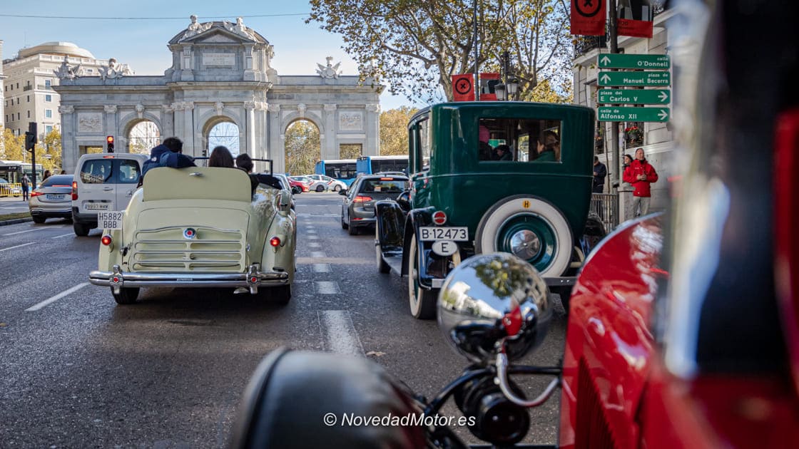 Caravana de coches clásicos pasando frente a la Puerta de Alcalá en la ruta de Autopía en Brocante
